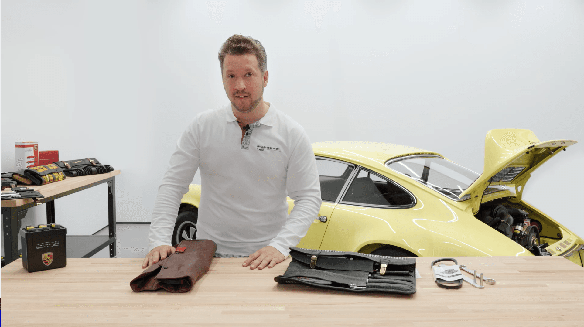 man is standing in front a table with different tool bags on it and a yellow historic 911 in the background