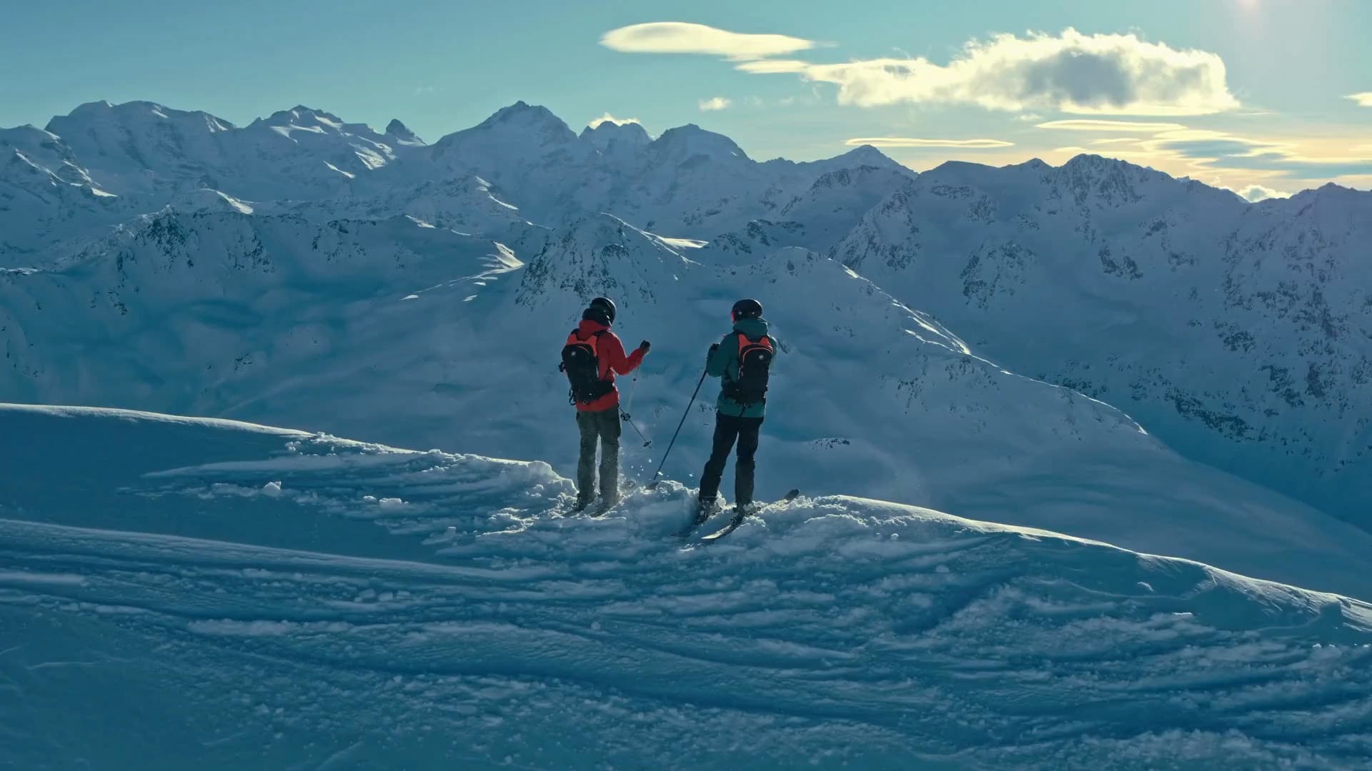 Two persons are standing in the snowy mountains with their ski