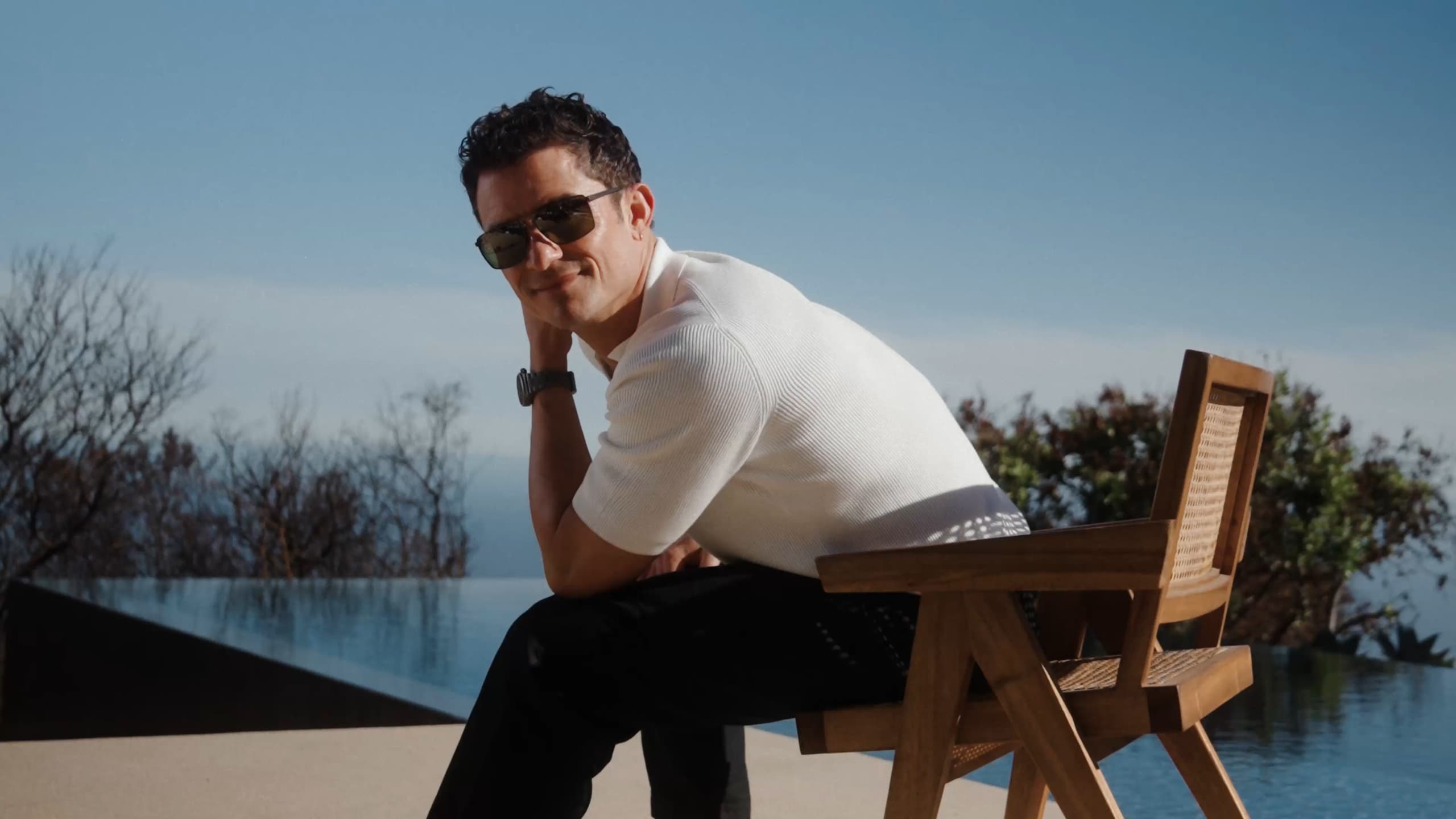 Orlando Bloom wearing Porsche Design Sunglasses sitting on chair next to a pool