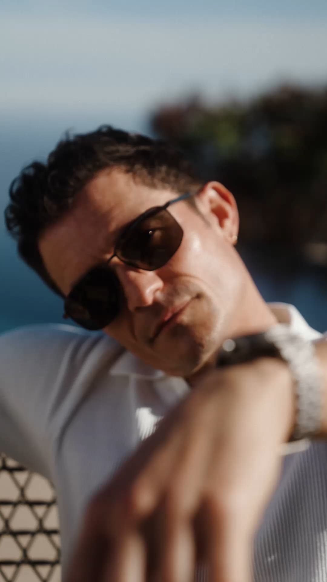 Orlando Bloom wearing Porsche Design Sunglasses sitting on chair next to a pool