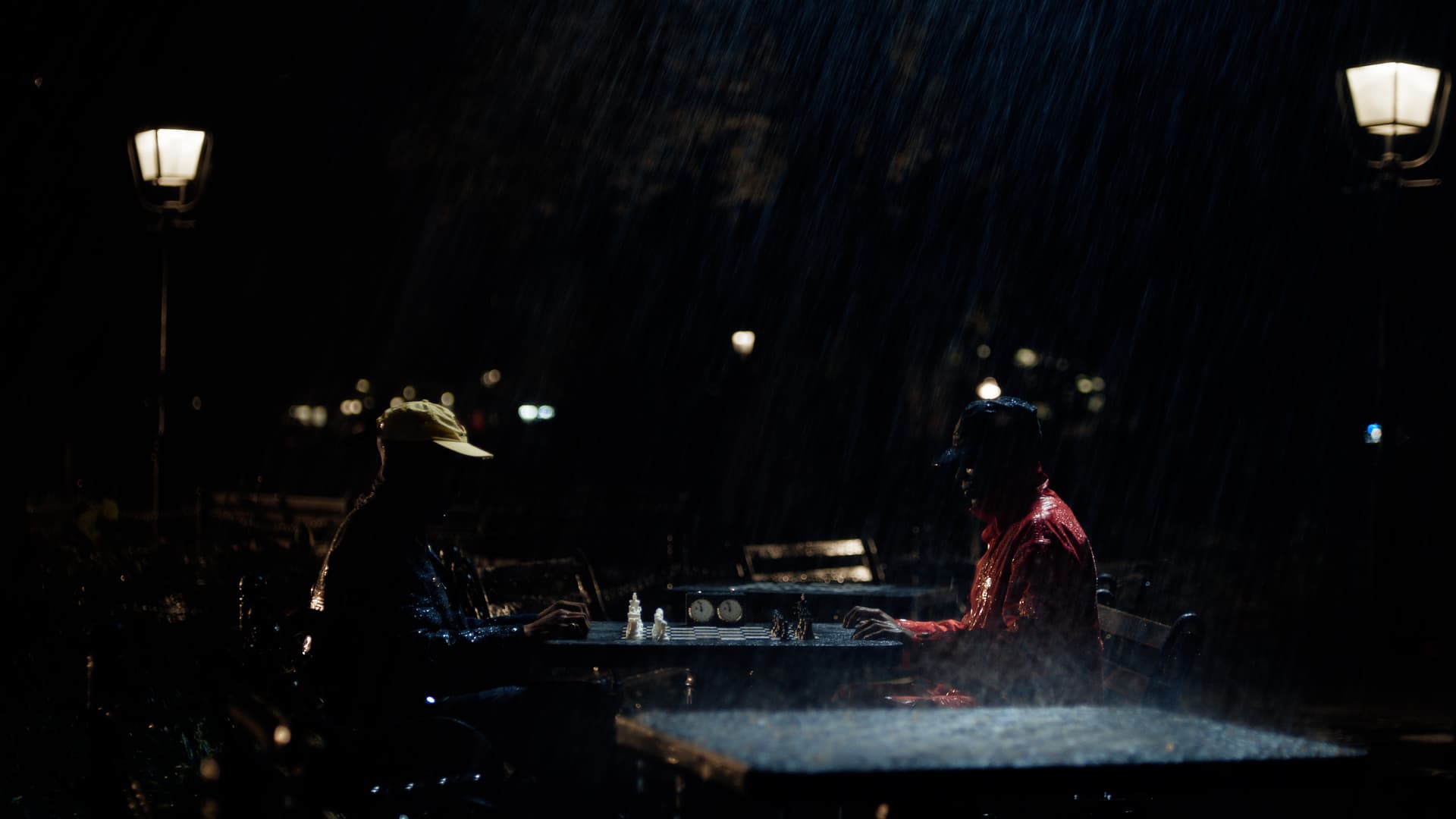 Two men sitting at a chess table in the rain in the dark