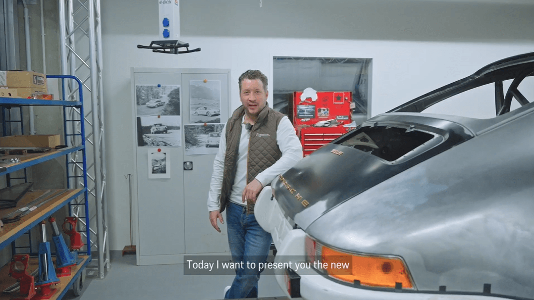 man in a garage next to a historic Porsche car
