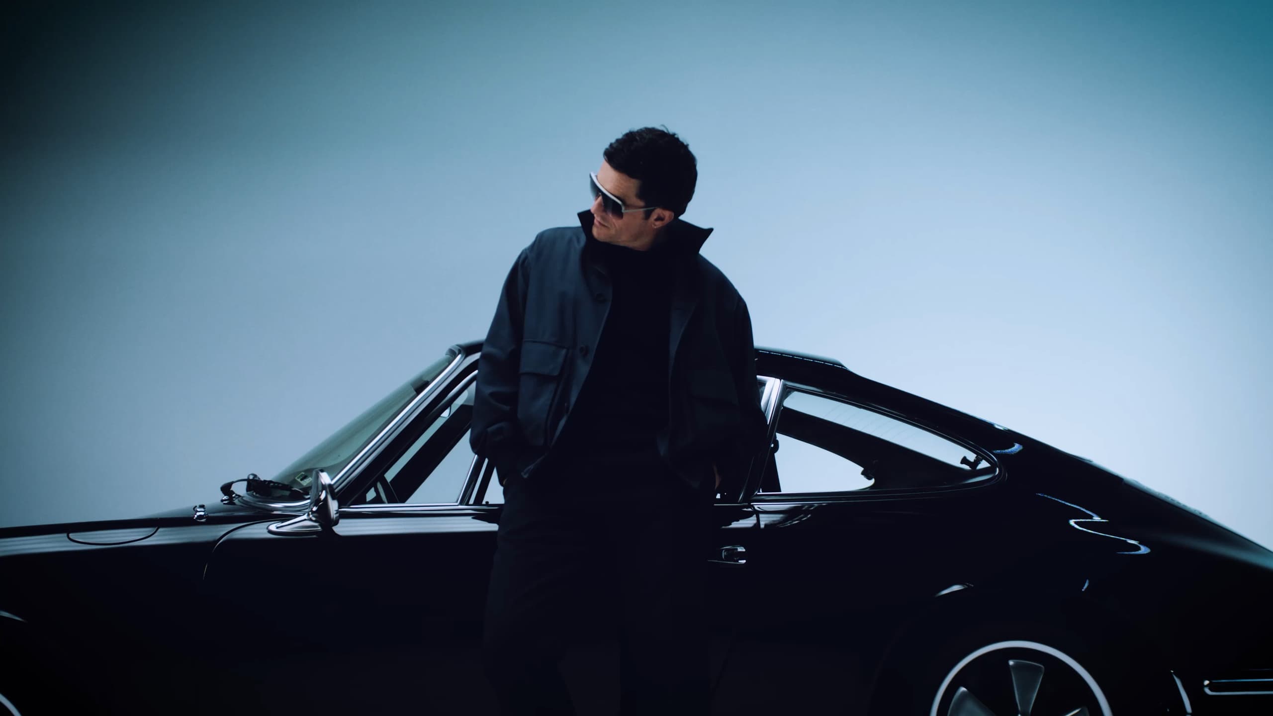 Orlando Bloom wearing Porsche Design Iconic Targa Sunglasses standing in front of a Porsche 911 Targa