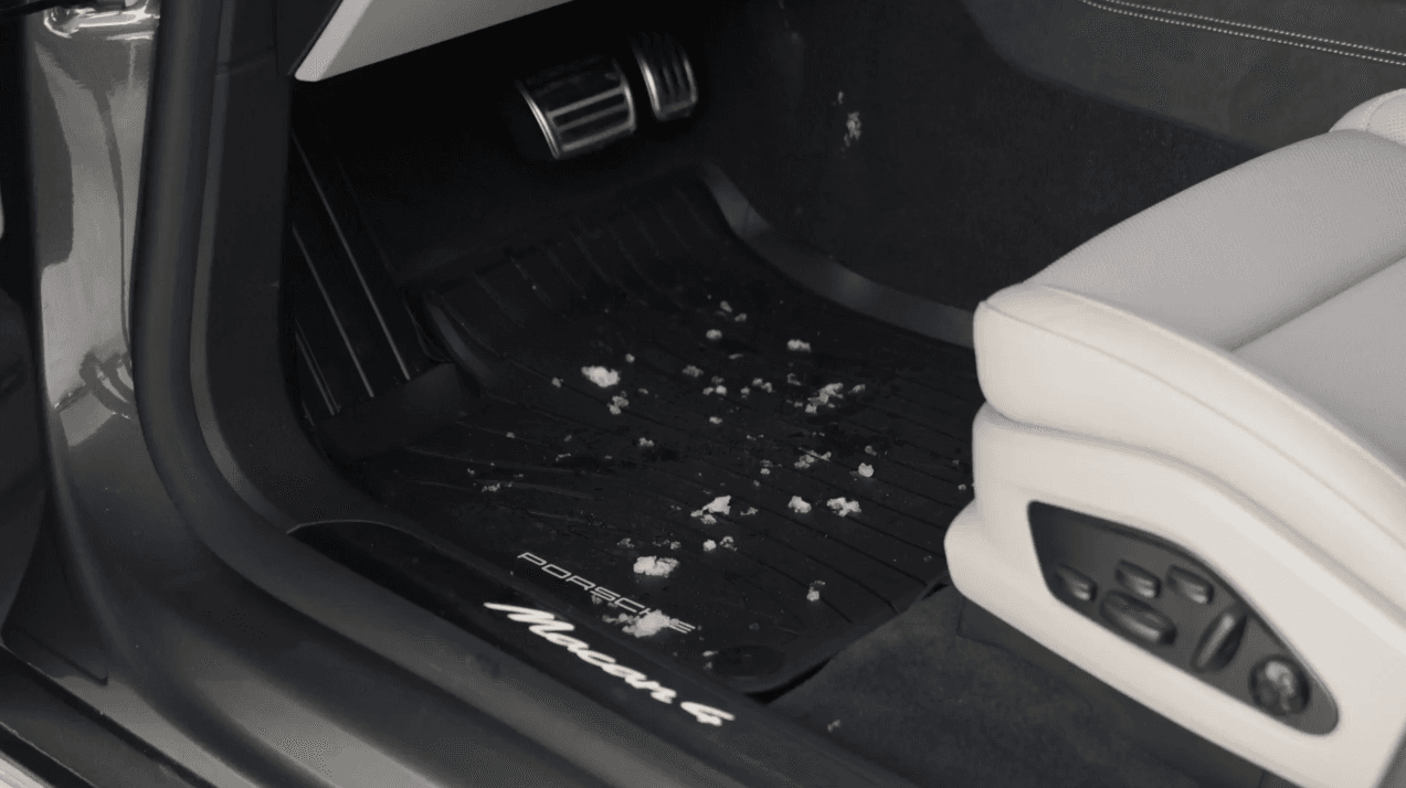 Car floor mat with snow debris, black mat with Porsche logo, beige seat visible, interior of a Porsche Macan
