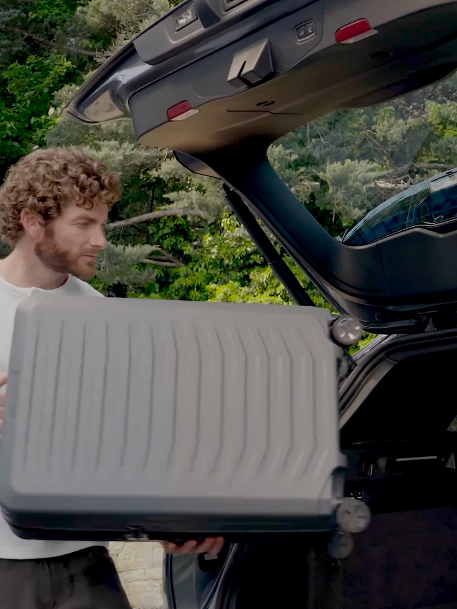 A man is carrying a black Porsche Design suitcase into the boot